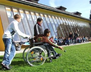 Educators can teach self-advocacy skills to students in a variety of ways. This image shows an individual in a wheelchair with two others on a grassy lawn.