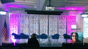 Stage at 1871 Chicago event with six blue chairs and purple lights highlighting 1871 logos behind stage.