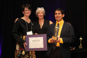 Ann, Jane, and Nestor stand together with the framed Awesome Award certificate.