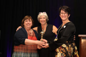 Marybeth of Evanston Community Foundation stands next to Jane and Ann with their new, gold Awesome Award statue.