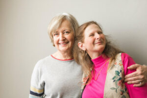 Jenny, in pink, poses with her mom who is wearing a gray shirt with red neck line.