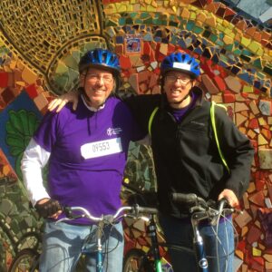 Caleb and his dad prepared for Bike the Drive together and stand in front of colorful mosaic wall