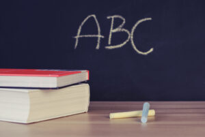 Image of a blackboard with letters ABC on it with books and chalk in the foreground.