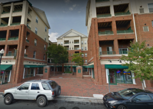 A tan and beige apartment structure with green awnings over businesses