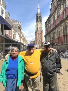 Three adults stand in the middle of a street in front of intricate European-style buildings