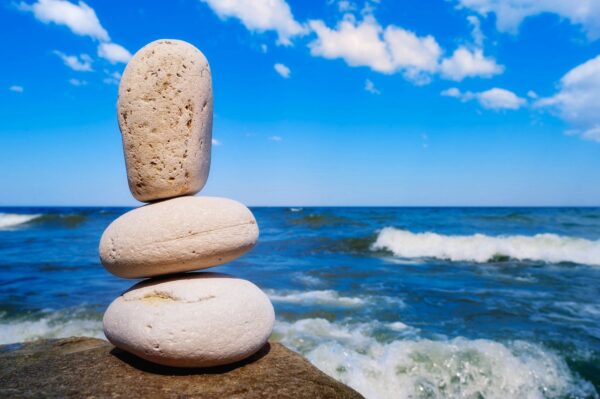 three balancing rocks in the foreground and an ocean view with blue skies and clouds in the background