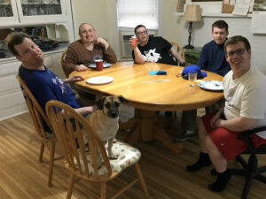 A group of roommates sit around a kitchen table.